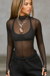 Front view of model posing in the fitted and sheer black mesh Exposed Seams Long Sleeve top with a mock neckline and exposed seam details