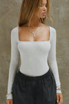 Front view of model posing in the fitted and stretchy pearl grey rib Square Neck Long Sleeve top with a wide square neckline