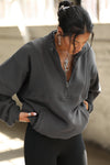 Front view of model posing in the oversized comfortable charcoal luxe french terry Retro Half Zip pullover sweatshirt with ribbed accents on the chest and sleeves, a hidden kangaroo pocket and a half zip collar