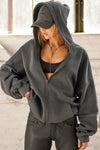 Front view of model posing in the oversized comfortable washed black french terry Oversized Zip Hoodie with a full length front zip closure, side pockets and thumbholes in the fitted cuffs