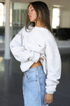 Side view of model posing in the soft oversized pearl grey french terry Classic Crew Pullover sweatshirt with a crew neckline and joah brown logo patch sewn on the upper left chest