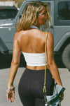 Back view of model posing outside in the street in the cropped and fitted white flexrib Halter Crop Tank with a banded scoop neckline.