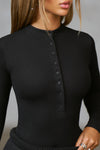 Close up front view of model posing in the fitted and stretchy black rib Button Down Henley long sleeve top with a high crew neckline and front buttons that reach about halfway down the shirt