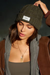 Front view of model posing in the soft and warm moss Cable Knit Beanie that has a custom JOAH BROWN "Dreamer" logo patch on the front