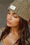 Front view of model posing in the soft and warm oak Cable Knit Beanie that has a custom JOAH BROWN 