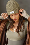 Front view of model posing in the soft and warm oak Cable Knit Beanie that has a custom JOAH BROWN 