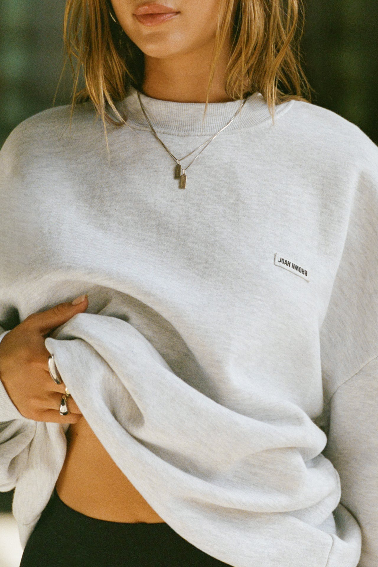 Close up front view of model posing in the soft oversized pearl grey french terry Classic Crew Pullover sweatshirt with a crew neckline and joah brown logo patch sewn on the upper left chest