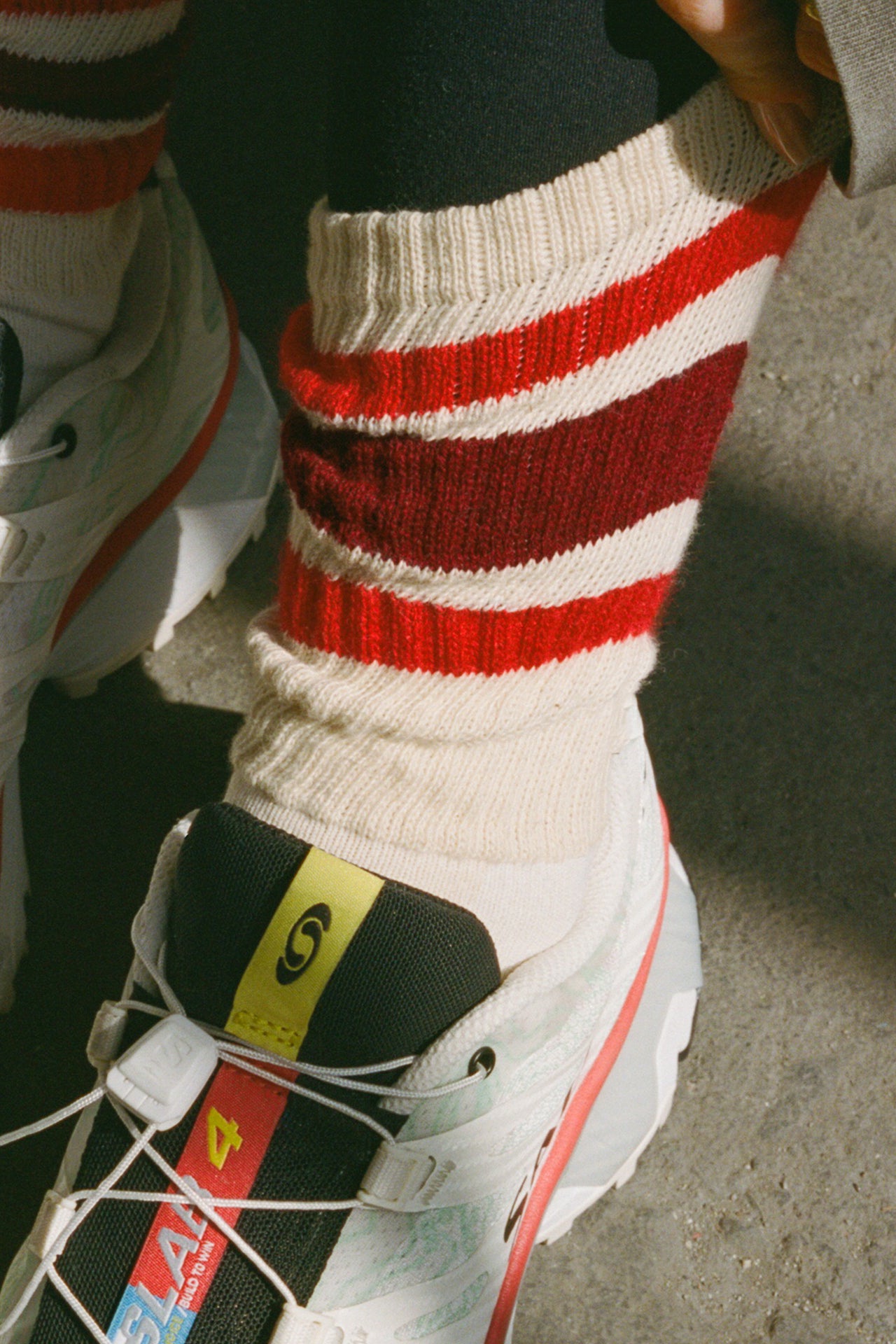 Close up front view of model adjusting the crew style ribbed soft red burgundy Classic Stripe Sock