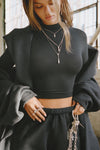 Front view of model posing in the fitted soft black modal Cropped Mock Neck Long Sleeve top with a raw cut hem