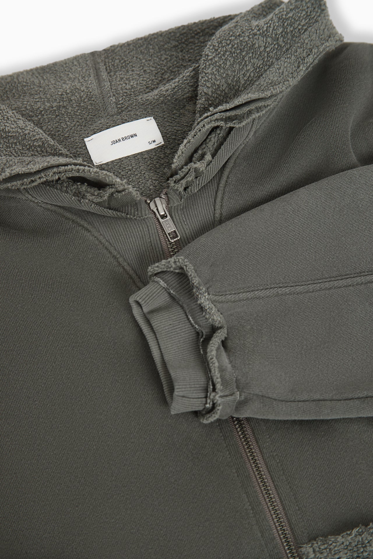 Close up flat lay front view of the loose-fit cropped washed sage french terry Deconstructed Crop Zip Hoodie with exposed seams and a JOAH BROWN logo patch on the sleeve