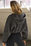 Back view of model posing in the loose-fit cropped washed black french terry Deconstructed Crop Zip Hoodie with exposed seams and back panel