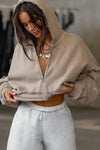 Front view of model posing in the loose-fit cropped sand french terry Deconstructed Crop Zip Hoodie with exposed seams and a JOAH BROWN logo patch on the sleeve