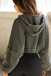 Back view of model posing in the loose-fit cropped washed sage french terry Deconstructed Crop Zip Hoodie with exposed seams and back panel