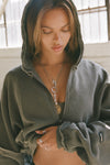 Front view of model posing in the loose-fit cropped washed sage french terry Deconstructed Crop Zip Hoodie with exposed seams and a JOAH BROWN logo patch on the sleeve