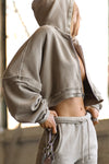 Side view of model posing in the loose-fit cropped sand french terry Deconstructed Crop Zip Hoodie with exposed seams and back panel details