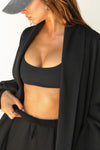 Close up front view of model posing in the knee-length loose fitting black french terry Oversized Cardigan with a rolled neckline and extra long sleeves