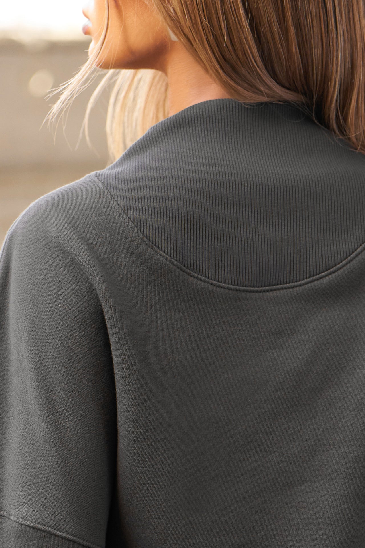 Close up back view of model posing in the charcoal luxe french terry Dolman Pullover sweatshirt with oversized sleeves, a mock neckline, curved hem and ribbed panels at the front and back