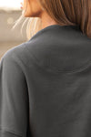 Close up back view of model posing in the charcoal french terry Dolman Pullover sweatshirt with oversized sleeves, a mock neckline, curved hem and ribbed panels at the front and back