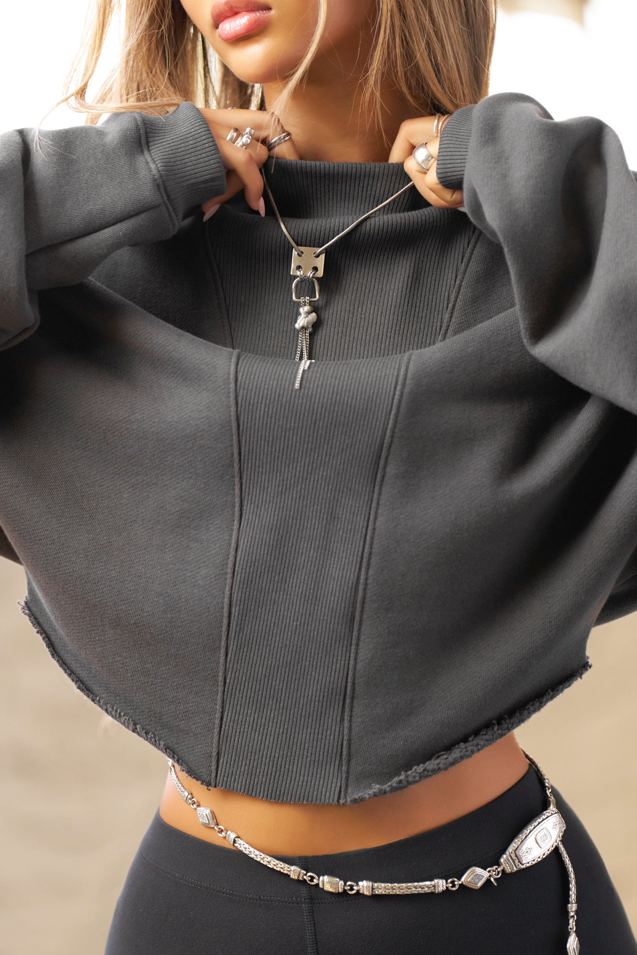 Close up front view of model posing in the charcoal luxe french terry Dolman Pullover sweatshirt with oversized sleeves, a mock neckline, curved hem and ribbed panels at the front and back