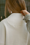 Close up back view of model posing in the off white french terry Dolman Pullover sweatshirt with oversized sleeves, a mock neckline, curved hem and ribbed panels at the front and back