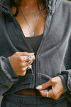 Close up detail front view of model posing in the loose-fit cropped washed black french terry Deconstructed Crop Zip Hoodie with exposed seams and a JOAH BROWN logo patch on the sleeve