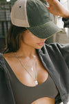 Side view of model posing the trucker style green/khaki Mesh Back Cap with a curved brim and stitched eyelets. Features a mesh back, snap-back closure and an embroidered Joah Brown logo on the front.