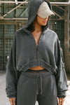 Front view of model posing in the loose-fit cropped washed black french terry Deconstructed Crop Zip Hoodie with exposed seams and a JOAH BROWN logo patch on the sleeve