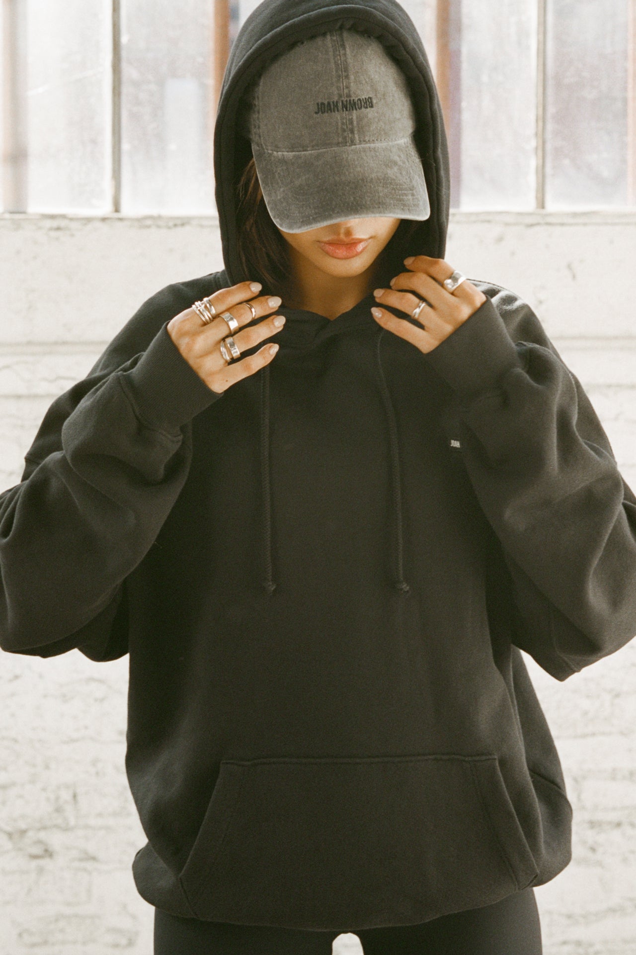 Front view of model posing in the oversized comfortable black french terry Oversized Pullover Hoodie sweatshirt with a Joah Brown logo patch at the front left chest, kangaroo pocket, drawstrings and thumbholes