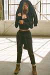 Full body front view of model posing in the tapered black french terry Empire Jogger with side pockets and an elastic waistband and ankle cuffs