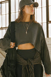 Front view of model posing in the cropped relaxed fit washed black cotton slouchy crop long sleeve top with a crew neckline, dropped shoulders and oversized sleeves