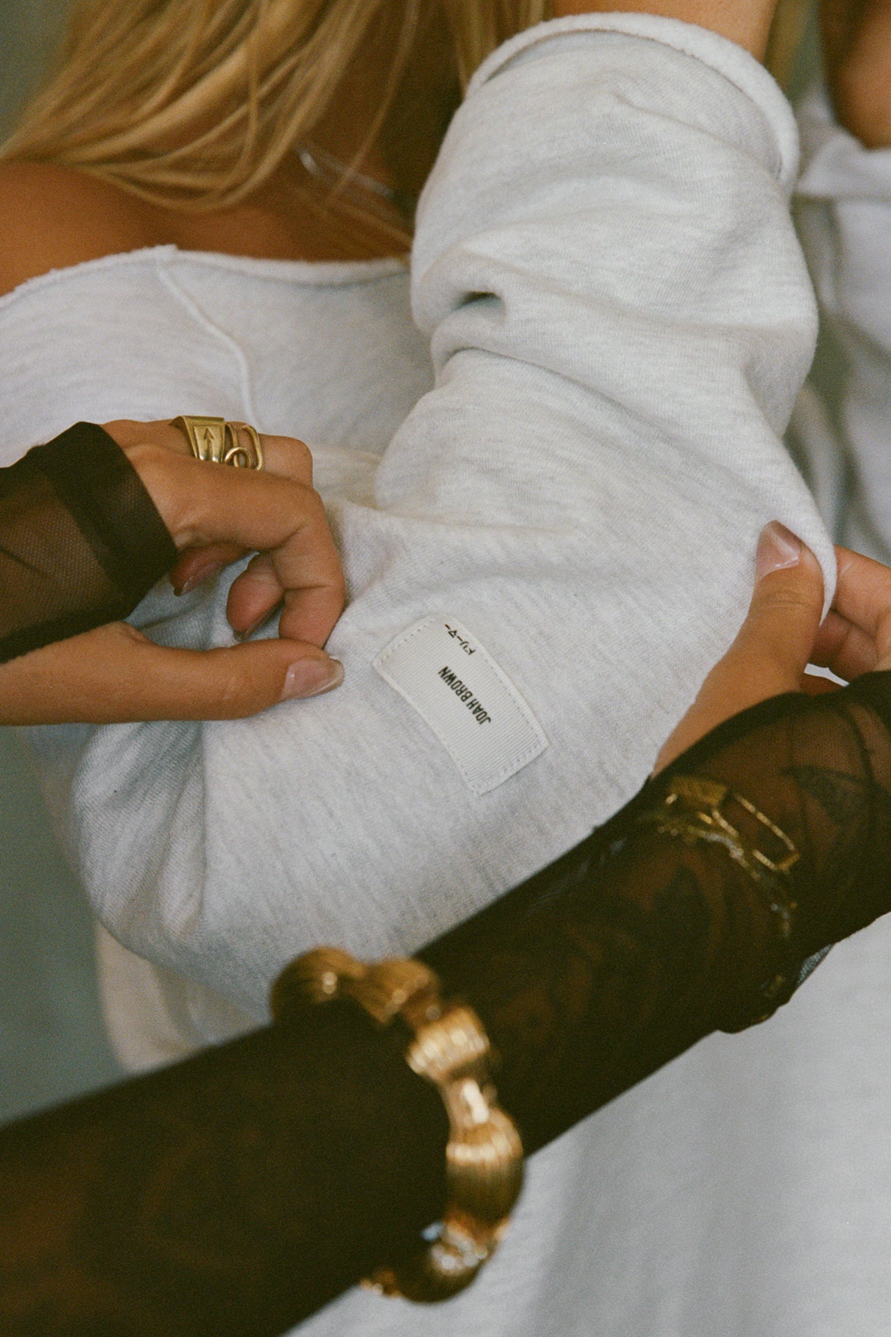 Close up detail side view of model posing in the oversized pearl grey french terry Slouchy Pullover Sweatshirt with a wide, off-the-shoulder neckline and a JOAH BROWN logo patch on the right sleeve