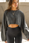 Front view of model posing in the cropped relaxed fit washed black cotton slouchy crop long sleeve top with a crew neckline, dropped shoulders and oversized sleeves