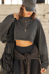 Front view of model posing in the cropped relaxed fit washed black cotton slouchy crop long sleeve top with a crew neckline, dropped shoulders and oversized sleeves