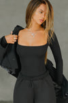 Front view of model posing in the fitted and stretchy black rib Square Neck Long Sleeve top with a wide square neckline