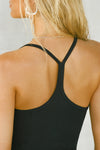 Close up detail back view of model posing in the fitted black flexrib Classic Racerback Tank with thin straps and a narrow racerback silhouette