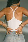Back view of model posing in the fitted white flexrib Classic Racerback Tank with thin straps and a narrow racerback silhouette