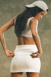 Back view of model posing in the fitted, soft natural luxe knit Foldover Mini Skirt with a fold-over waist band that can be worn high, mid or low rise