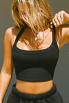 Front view of model posing in the cropped and fitted black flexrib Halter Crop Tank with a banded scoop neckline.