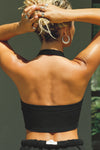 Back view of model posing in the cropped and fitted black flexrib Halter Crop Tank with a banded scoop neckline.