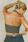 Back view of model posing in the cropped and fitted mineral flexrib Halter Crop Tank with a banded scoop neckline.