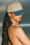 Side view of model wearing the six-panel khaki with vintage blue brim Official Cap with a curved brim and an embroidered upside down Joah Brown logo on the front