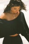  Front view of model posing in the street wearing the cropped, loose fitting black modal Relaxed Crop Long Sleeve top with a wide scoop neckline that can be worn off the shoulder