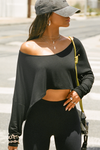  Front view of model posing in the street wearing the cropped, loose fitting black modal Relaxed Crop Long Sleeve top with a wide scoop neckline that can be worn off the shoulder