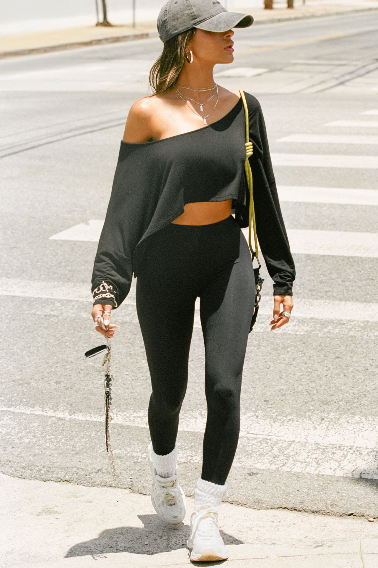  Full body front view of model posing in the street wearing the cropped, loose fitting black modal Relaxed Crop Long Sleeve top with a wide scoop neckline that can be worn off the shoulder