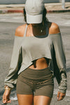  Front view of model posing in the street wearing the cropped, loose fitting sage modal Relaxed Crop Long Sleeve top with a wide scoop neckline that can be worn off the shoulder