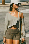 Front view of model posing in the street wearing the cropped, loose fitting sage modal Relaxed Crop Long Sleeve top with a wide scoop neckline that can be worn off the shoulder