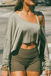 Close up front view of model posing in the street wearing the cropped, loose fitting sage modal Relaxed Crop Long Sleeve top with a wide scoop neckline that can be worn off the shoulder