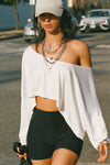 Front view of model posing in the street wearing the cropped, loose fitting white modal Relaxed Crop Long Sleeve top with a wide scoop neckline that can be worn off the shoulder