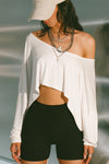 Front view of model posing in the street wearing the cropped, loose fitting white modal Relaxed Crop Long Sleeve top with a wide scoop neckline that can be worn off the shoulder