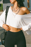 Close up front view of model posing in the street wearing the cropped, loose fitting white modal Relaxed Crop Long Sleeve top with a wide scoop neckline that can be worn off the shoulder